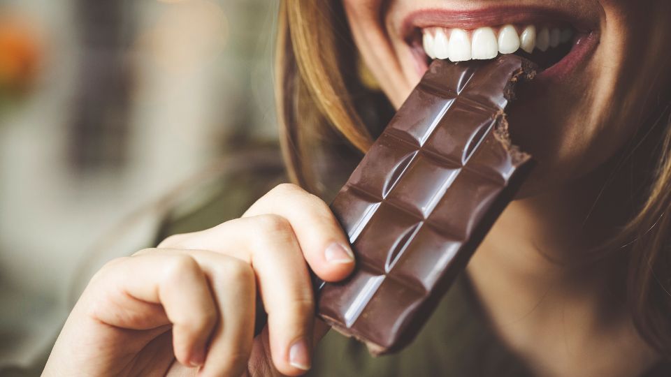 femme tenant une tablette de chocolat dans sa bouche en souriant